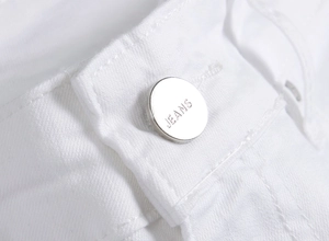 Macro shot of the white denim waistband featuring a silver metal button with Jeans engraving