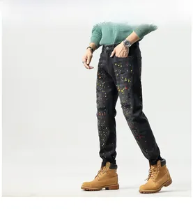 Detail of slim-fit black denim jeans with artistic multicolor paint splatter and distressed effects