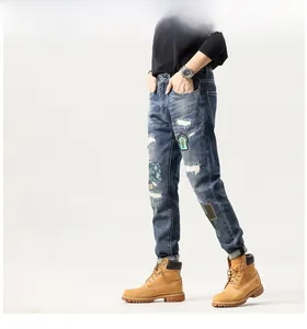 Detailed view of men's distressed blue denim jeans with embroidery patches and biker details