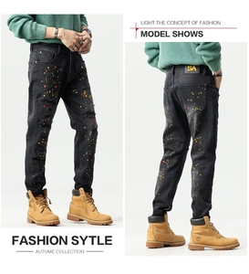 Detail of slim fit black jeans featuring distressed holes and colorful paint splatter
