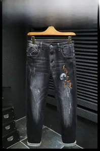 Détail de la broderie artistique sur un jean en denim noir avec lavage vintage et revers chic
