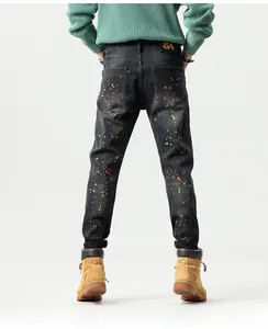 Detail view of black slim-fit jeans with colorful paint splatter and logo leather patch