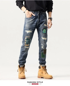 Detail shot of men's distressed blue denim jeans with embroidery patches and biker repairs