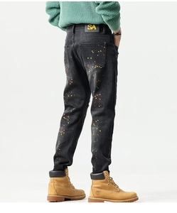 Detail view of black slim-fit denim jeans with vibrant paint splatter and rear leather patch
