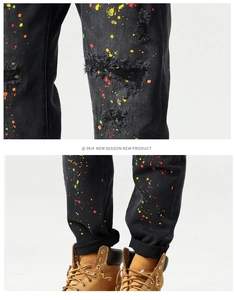 Close-up of distressed black slim fit jeans with colorful paint splatters and ripped knees