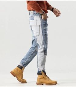 Detail shot of men's jeans showing asymmetric color-block patchwork and distressed denim texture