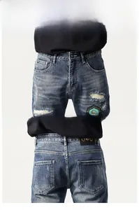 Detail of dark blue denim jeans featuring distressed patchwork and badge embroidery