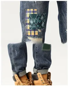 Detail of blue distressed denim jeans with tartan plaid patches and rolled-up cuffs