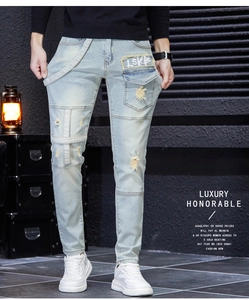 Detail of distressed light blue denim with frayed patches and decorative straps on men's jeans