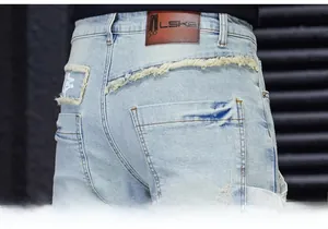 Detail view of denim jeans featuring a brown leather patch and distressed pocket stitching