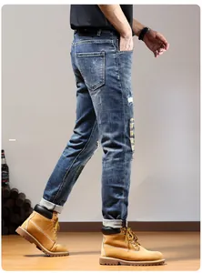 Detail of distressed denim jeans featuring unique plaid patches and embroidery on dark blue fabric