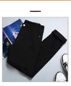 Vue détaillée de jean noir usé avec déchirures à franges et finitions de couture rouge