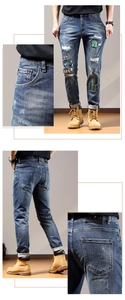 Detailed view of distressed men's jeans with vintage patchwork and embroidery accents