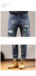 Close-up of ripped blue denim jeans with green embroidery patch and cat whisker texture