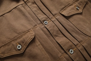Close-up of heavy brown canvas work jacket with dual flap pockets and metal buttons