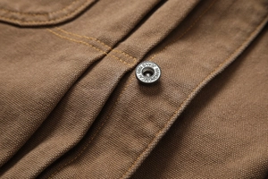 Macro detail of silver metal button and double stitching on brown canvas work jacket
