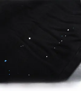 Détail du tissu denim noir avec des éclaboussures de peinture bleue et blanche