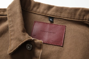 Detail of vintage canvas jacket showing leather logo patch and size label on inner neck
