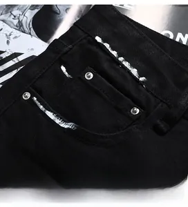 Détail de la poche avant d'un jean noir avec peinture graffiti blanche et rivets en métal