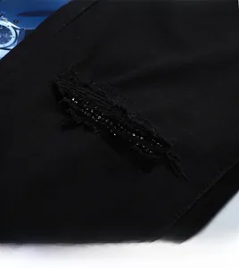 Détail macro de jean noir pour homme avec broderie à paillettes et bords effilochés