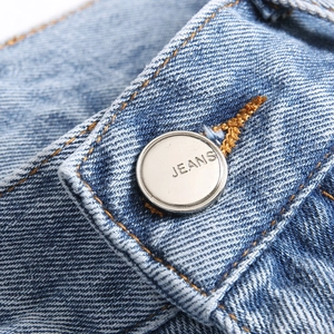 Gros plan sur le bouton métallique gravé et les coutures brunes du jean bleu