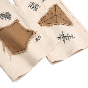 Close-up of men's slim-fit cream trousers featuring artistic raw-edge patch and embroidery