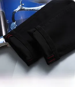 Gros plan sur l'ourlet du jean noir avec double surpiqûre rouge décorative et texture sergée