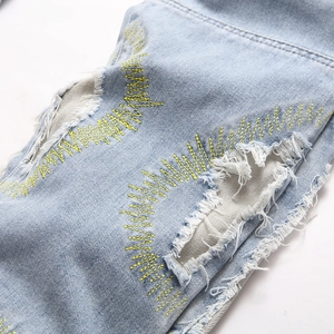 Distressed light blue slim fit jeans featuring yellow zigzag embroidered hole details