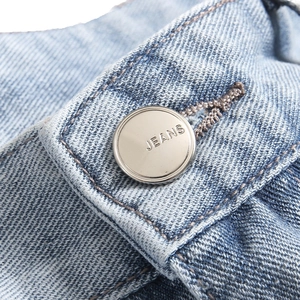 Detail of light blue denim jeans with high-quality silver metal button and precise stitching