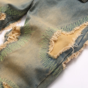 Distressed vintage blue men's jeans with ripped holes and neon green zigzag embroidery