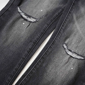 Detalle de tela vaquera gris con agujeros desgastados en rodillas y salpicaduras de pintura