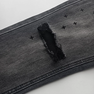 Distressed black denim jeans with cross print and ripped patches in retro street style