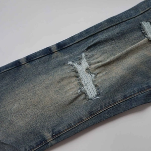 Detalle de vaqueros denim desgastados con lavado amarillo y costuras naranjas decorativas