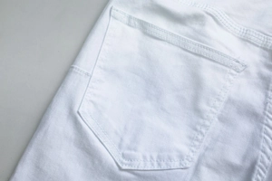 Macro view of white denim jeans back pocket showing twill texture and double stitching