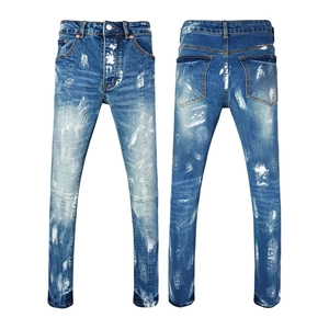 Close-up of distressed blue denim fabric with white paint splatter and faded wash details