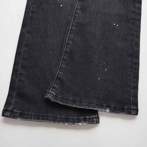 Detalle de vaqueros denim gris oscuro con salpicaduras blancas y bajos deshilachados
