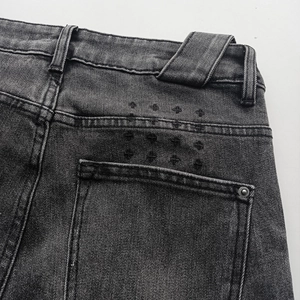 Detail of dark gray denim jeans showing back pocket and unique cross star embroidery
