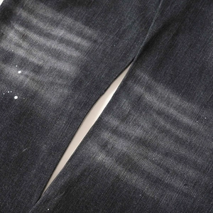 Detalle de denim negro desgastado con lavado vintage y textura de pintura blanca