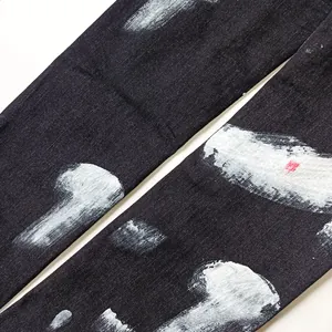 Detail of slim-fit black jeans featuring unique white paint splatter texture on denim