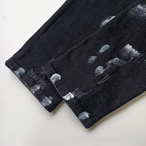 Detail of black slim denim jeans cuff with white paint spray graffiti and distressed edges