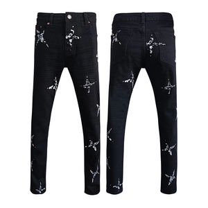 Detail of slim-fit black denim jeans featuring white cross star and paint splatter prints