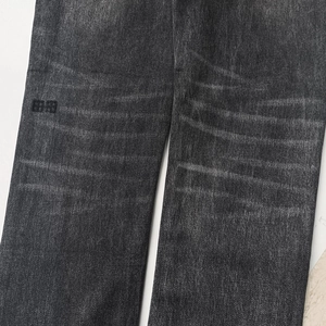 Detail of dark grey distressed denim showing whiskering effect and square embroidery