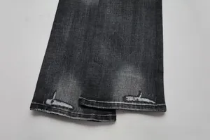 Close-up of distressed hem on dark grey slim-fit flared jeans with vintage frayed details