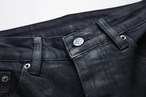 Detailansicht des Bundes einer schwarzen Jeans mit silbernem Metallknopf und Nieten