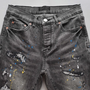 Detailed shot of dark grey distressed denim with artistic paint splatters and studs