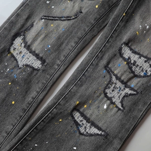 Detailed close-up of dark grey distressed denim with ripped patches and paint splatters