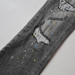 Detailed macro view of distressed black washed denim with paint splatters and ripped patches