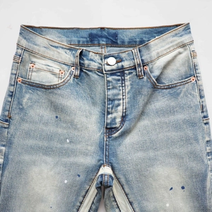 Detail of light blue washed denim jeans featuring artistic white paint splatter accents