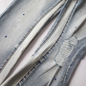 Detail of light blue washed denim with distressed knee rips and white paint splatter accents