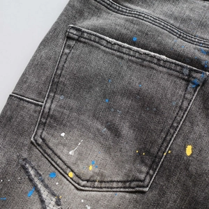 Close-up of distressed denim fabric featuring colorful paint splatter and stitching details